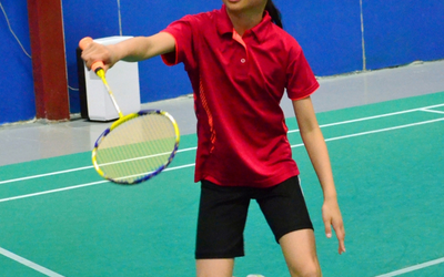 Vue rapprochée d'un jeune joueur sur un terrain vert de badminton, tenant une raquette et s'apprêtant à frapper le volant.