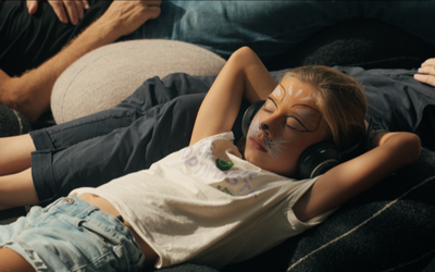 Sur cette image on voit une petite fille couchée sur des coussins. Elle a les yeux fermés et a un casque sur les oreilles.