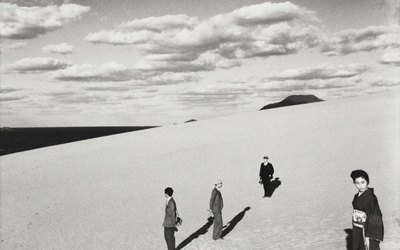 Photographie en noir et blanc, quatre personnages sur une dune de sable