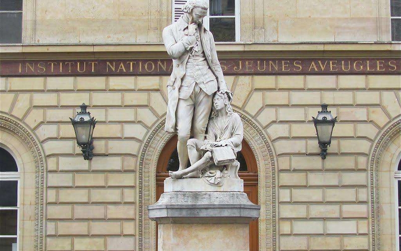 Statut blanche de Valentin Haüy devant la façade de l'inja louis braille.