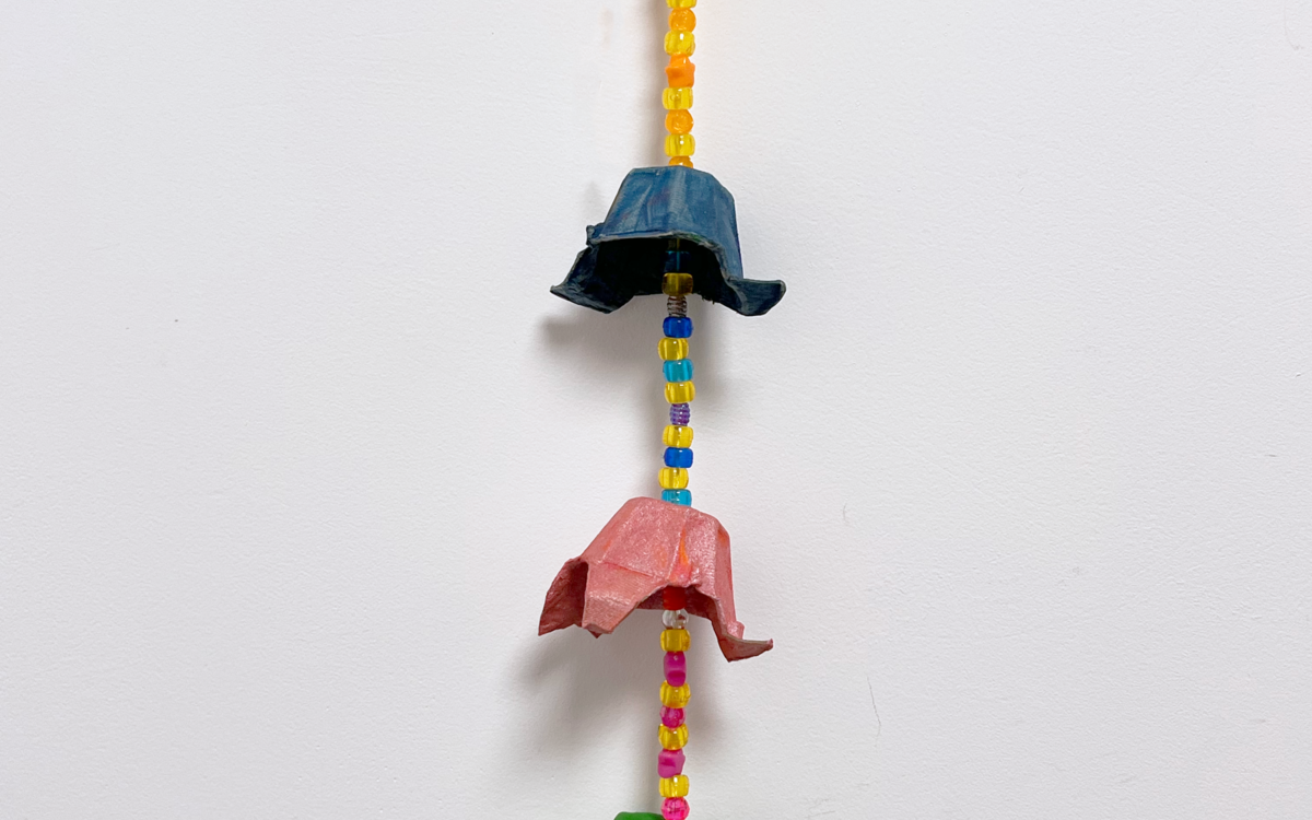 Photographie d'une suspension murale faite à partir de boîtes d'œufs peintes et de perles, le tout de différentes couleurs : rose, jaune, bleu, vert et orange.