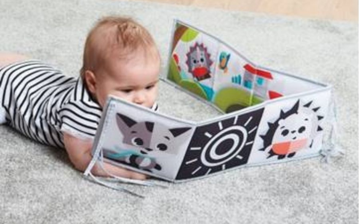 Un bébé devant un leporello sur un tapis doudou gris perle