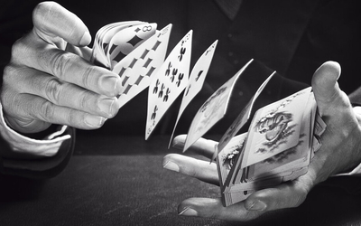 Visuel en noir et blanc représentant des mains qui jouent avec des cartes de jeu