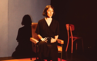Femme habillée en noir assise sur un fauteuil au milieu d'une scène de théâtre