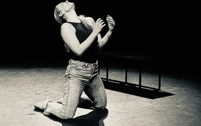 Photographie en noir et blanc où on voit une femme à genoux sur scène