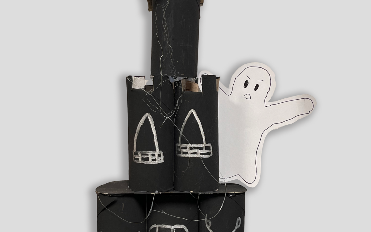 Un château hanté fabriqué et construit à la main. Le château est noir avec des détails blancs et un fantôme fait en papier. 