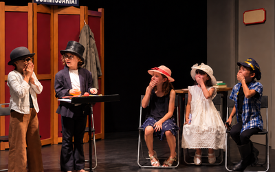 Enfants costumés jouant une scène de théâtre sur scène.