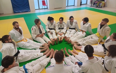 Des judokas sont assis en cercle qui forme comme une fleur. Ils sont les uns à côté des autres. Ce moment permet de partager avant de faire la séance. 