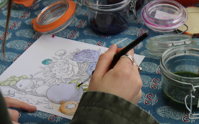 Photographie d'une main tenant un pinceau, en train de peindre un dessin de bouquet de fleurs avec de l'encre qui a été fabriquée à partir de végétaux. 