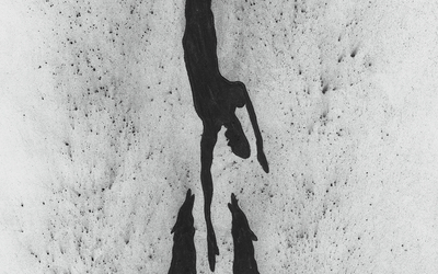 L'image représente un dessin au fusain d'un corps d'homme semblant chuter au milieu de deux loups, têtes levées vers le haut, attendant leur proie