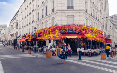 Jeune femme en robe sombre à pois blancs devant la brasserie fleurie "La Gaîté" à Montparnasse, photographiée par Yann Vaternelle, dans le cadre de son projet PAUSE - "Montparnasse : une histoire de rencontres" en collaboration avec l'hôtel Mercure Paris Centre Gare Montparnasse (vernissage et vente de tirages le mercredi 23 septembre de 17h à 21h)