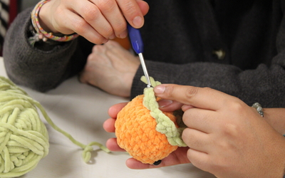 Photographie des mains d'une participante de l'atelier créatif peluche en crochet, en train de crocheter une mini orange.