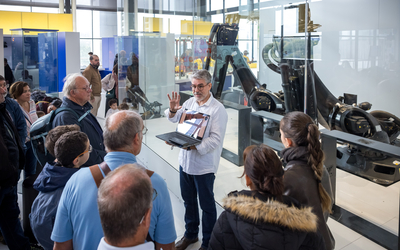 Homme tenant un ordinateur et parlant pour présenter ses recherches et la visite d'une exposition devant un groupe de participants