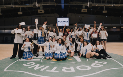 Groupe de jeunes danseuses et danseurs de Novakill Studio réunis dans une grande salle de sport à Paris. Les participants, vêtus de différentes tenues inspirées de la K-pop, sourient et brandissent des certificats devant un écran affichant le logo Novakill Studio.