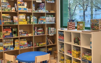photo d'une ludothèque en intérieur avec des jeux sur les étagères, une petite table avec des chaises pour les enfants et une fenêtre avec des arbres
