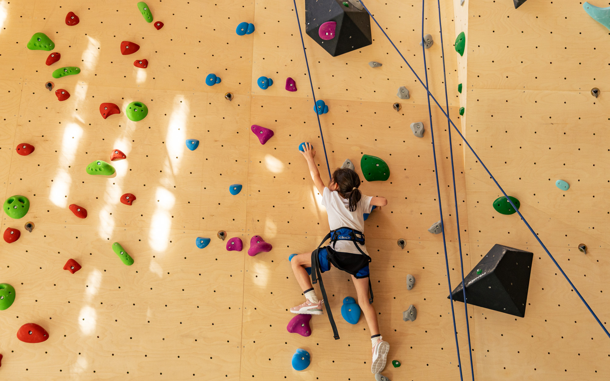 Une petite fille vue de dos grimpe sur un mur
