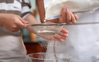 Deux femmes  versant de la farine dans un tamis dans la cuisine à la maison