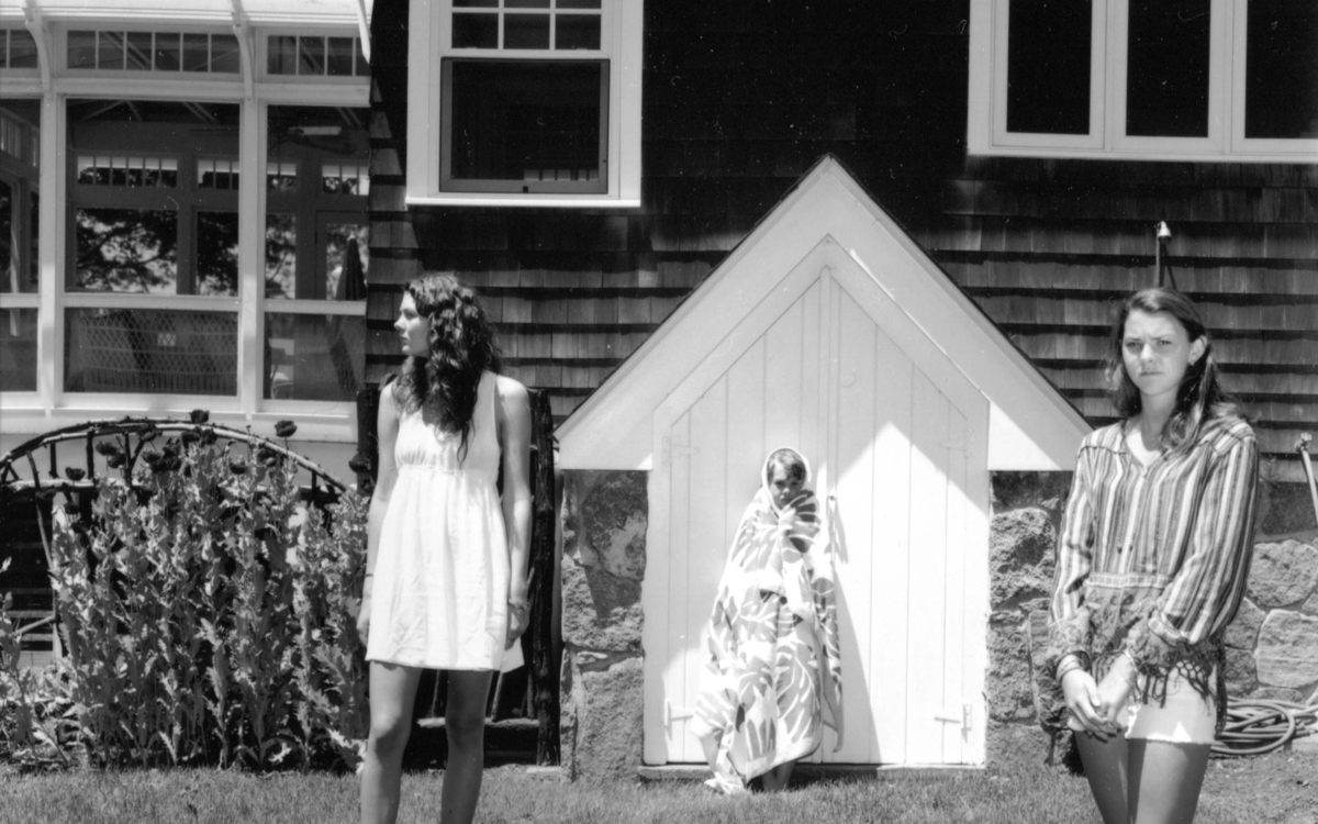 Photographie en noir et blanc représentant de deux femmes et d'un enfant devant une maison
