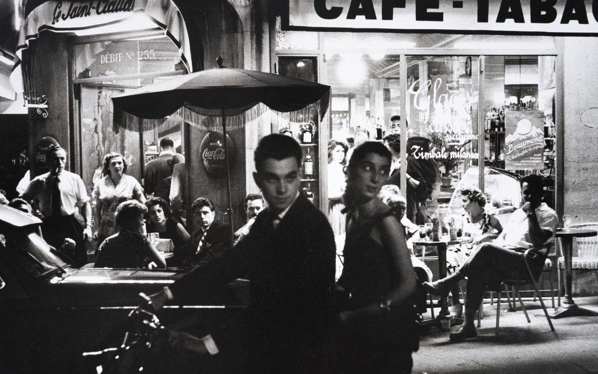 Photographie en noir et blanc d'un homme et d'une femme sur un scooter devant un café-tabac parisien